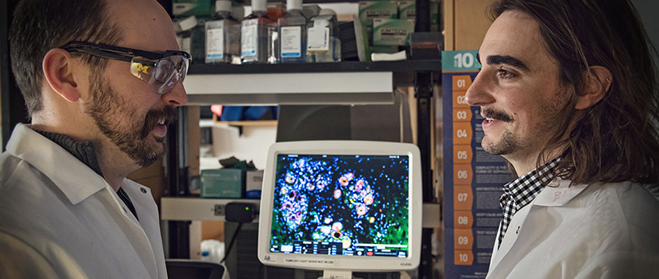 Costas Lyssiostis with member of his lab face one another in front of a computer