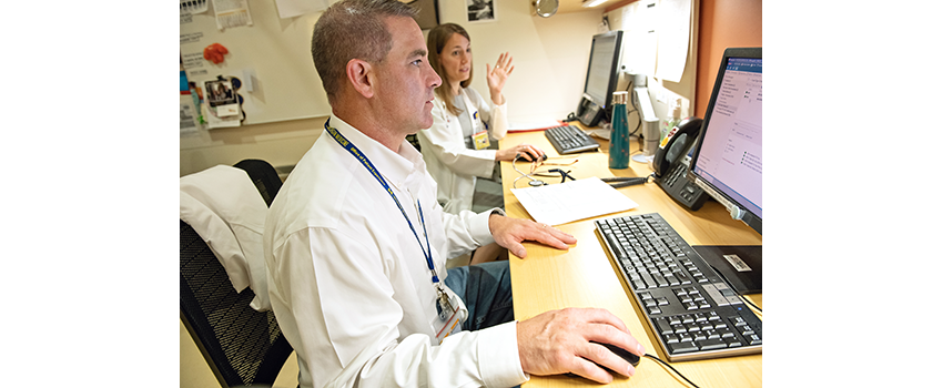 Dale Bixby sits at a computer with a colleague in the background