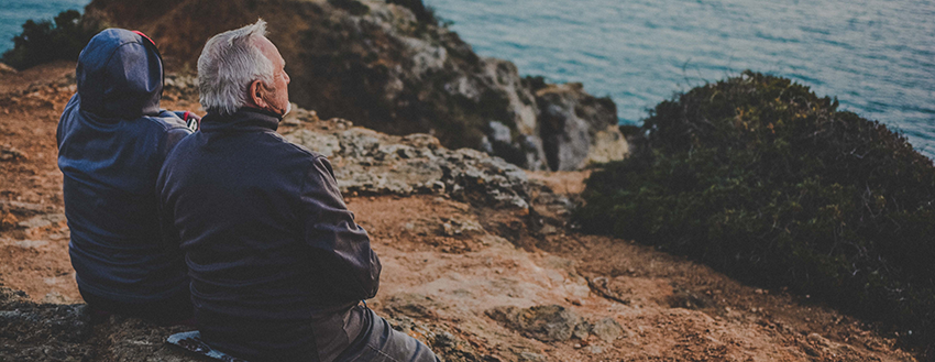 image of older couple sitting side-by-side along the coast