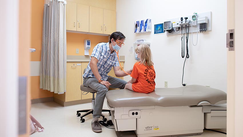 photo of doctor with a young patient in an exam room, using a stethoscope