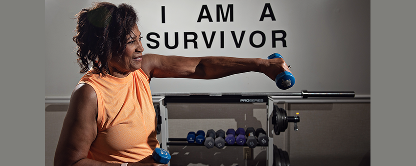 Jennifer Watson using free weights in front of an I am a survivor sign