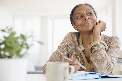 A woman sits with a writing pad, looking up and thinking