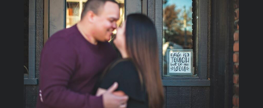 Couple standing in front of rustic-looking building embracing