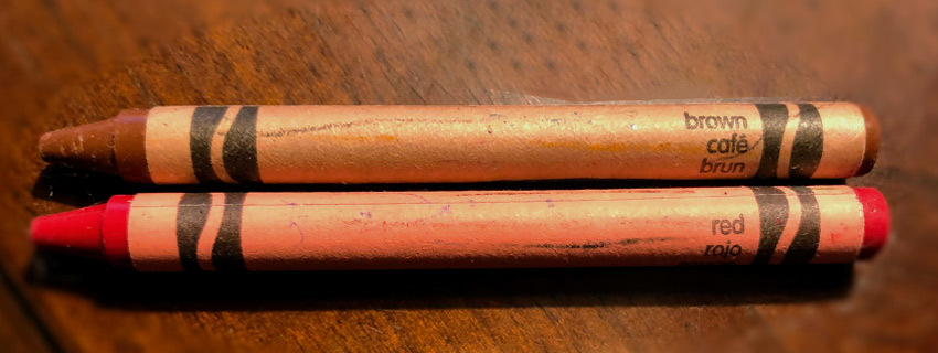 A brown and orange crayon side-by-side on a desk