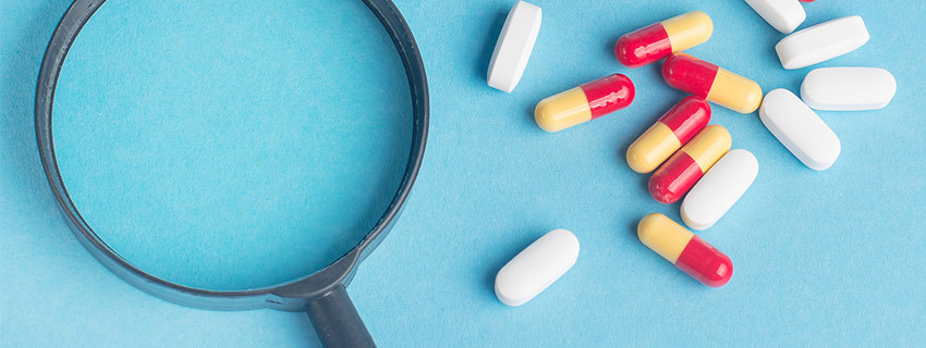 Magnifying glass next to a handful of pink and white capsules