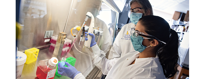 Two women wearing masks work together to study a specimen in a lab