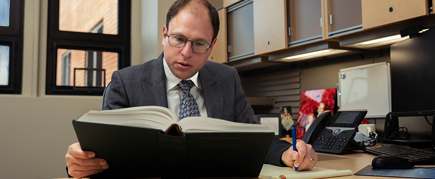 Andrew Shuman, M.D. sits at his desk reading a book