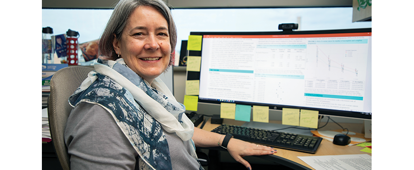 Celeste Leigh Pearce, Ph.D., M.P.H. sits in front of a computer