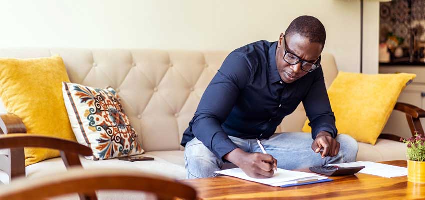 Black man sits on his couch studying his bills