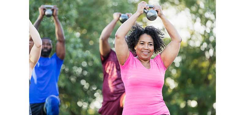 Black woman exercising with kettle bell along with others of different races