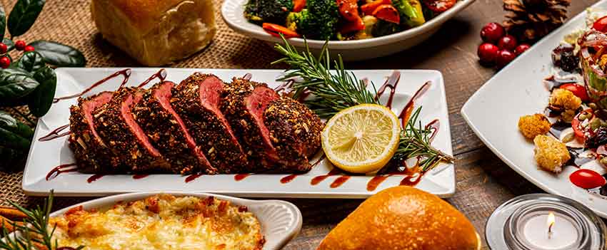 sliced roast surrounded by side dishes and evergreens