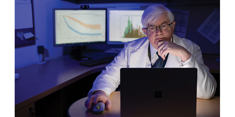 Charles Mayo, PhD is an older white man with glasses sitting in front of his computer