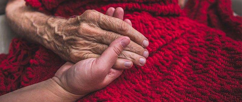 Close up of an older person holding a younger person's hand on a red blanket