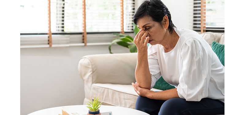 Older woman sits with fingers pressed against bridge of her nose