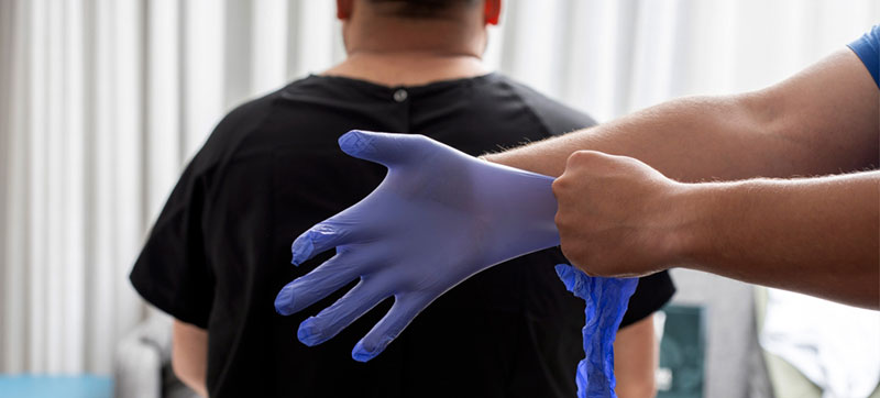 man sits in an exam room as a doctor pulls on a examination glove
