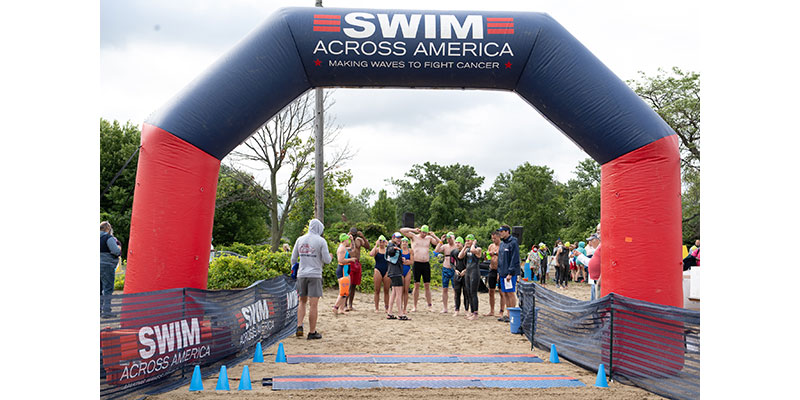 A large group of swimmers gathers under a banner preparing to start their swim
