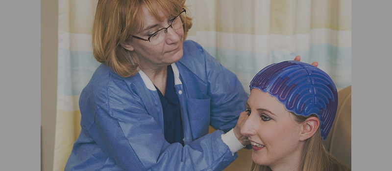 Nurse fitting a woman with a cold cap which is blue and fits snug to her head