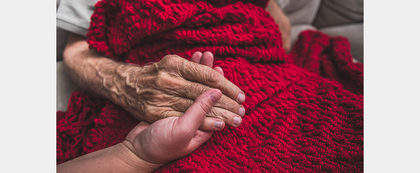 Senior hand holding younger hand against red blanket