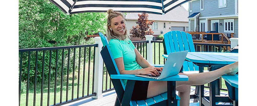 Koskinen smiles while working on her computer outside under an umbrella.
