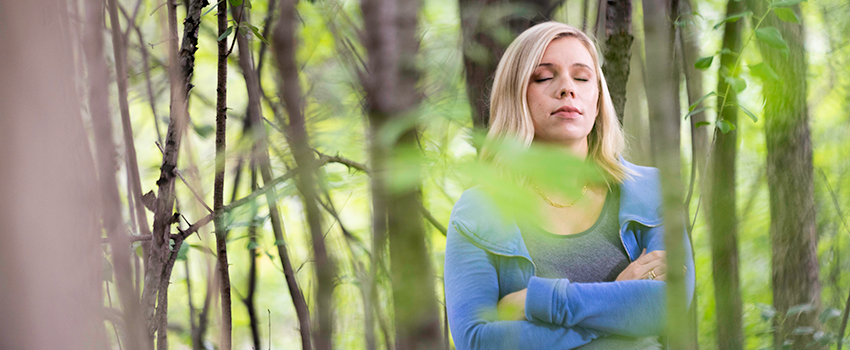 Leah Koskinen stands in the woods meditating