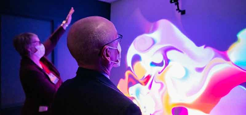 A man and woman stand in front of a glowing, colorful interactive screen